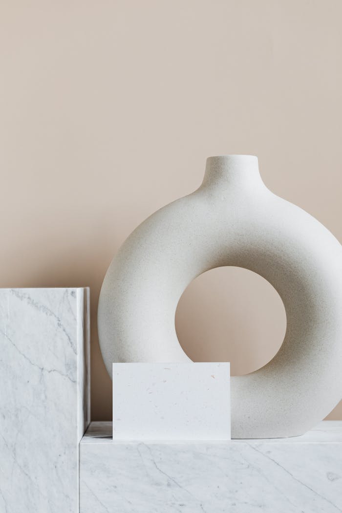 Original circular ceramic vase placed on marble cabinet against beige wall in modern minimalistic apartment